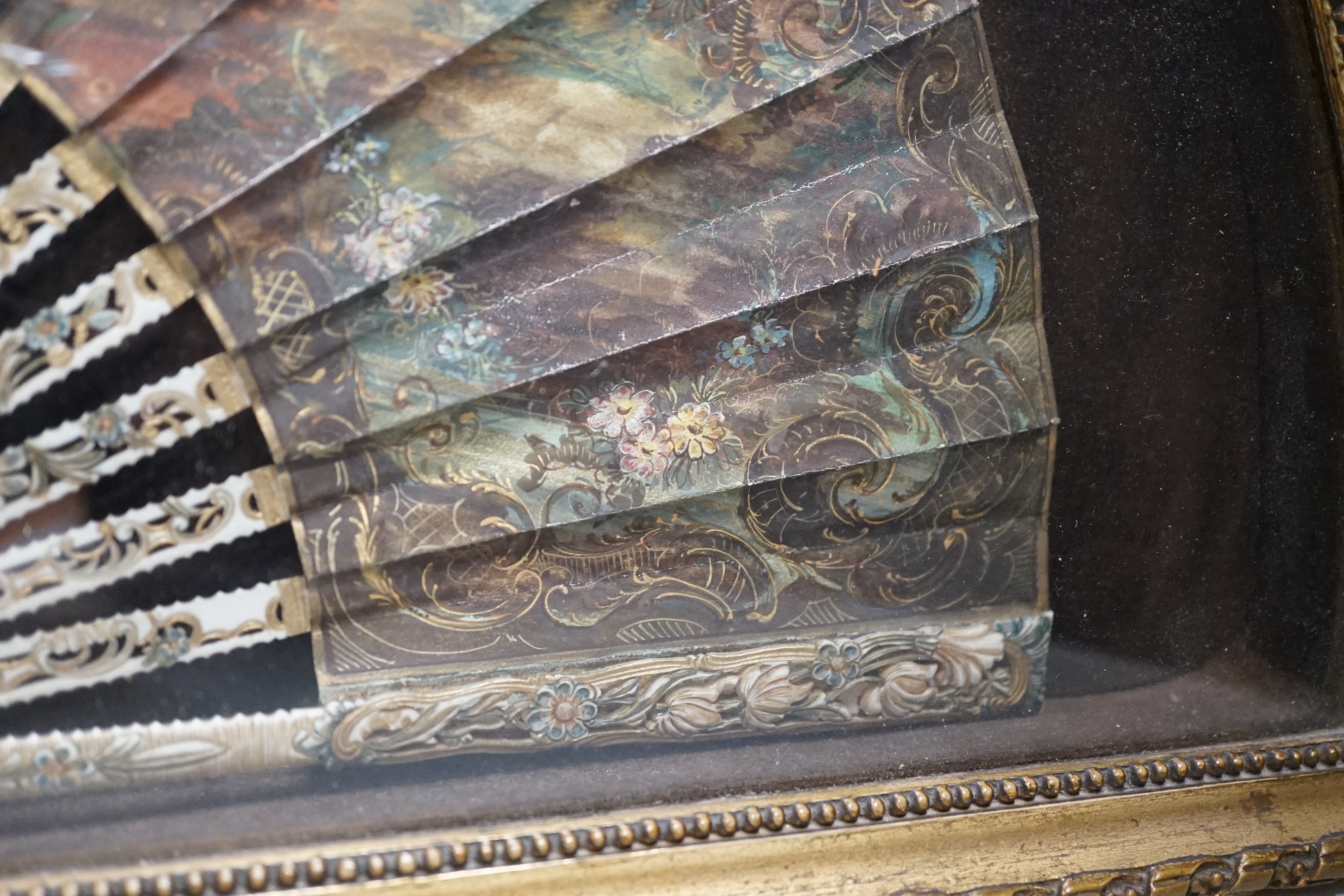 A 19th century French bone fan with pierced decoration, hand painted with figures wearing 18th century dress before a landscape, framed, the frame 62cm wide